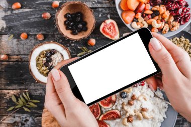 Kızın eller fotoğraf pilav Hindistan cevizi lapası incir, çilek, fındık ve Hindistan cevizi sütü ile smartphone tarafından çekici. Sağlıklı kahvaltı malzemeler. Yeme, vegan gıda kavramı temiz. Üstten görünüm