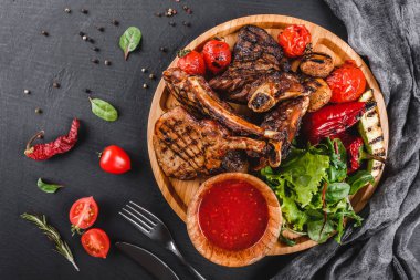 Siyah taş arka plan üzerinde kesme tahtası üzerinde taze salata ve barbekü sos ile kemik ve sebze Üzerinde Izgara Ribeye Steak. Sıcak Et Yemekleri. Üst görünüm, düz yatıyordu