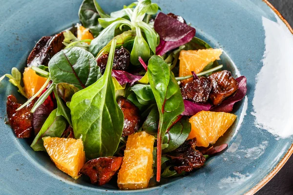 Salat mit Leber, Rucola, Orange, Spinat und Mandeln auf Teller über dunkler Steinoberfläche. Konzept für gesunde Ernährung. Ansicht von oben. — Stockfoto