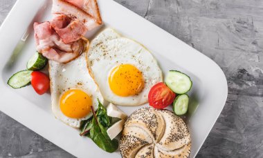 Kahvaltı, sahanda yumurta, topuz, sosis, pastırma, salam, plaka gri masa yüzeyi üzerinde taze salata. Sağlıklı gıda, üstten görünüm, düz yatıyordu