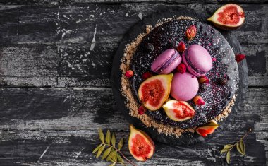 Aynalı kremalı çikolatalı pasta. Makaronlarla, incirlerle, koyu kırsal arka planda çiçeklerle süslenmiş. Tatil pastası kutlaması. Üst manzara, düz uzanma.