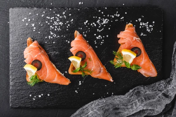 Förrätt bruschetta med filé lax, oliver och citron på ciabatta bröd på stone skiffer bakgrund. Hälsosam matkoncept. — Stockfoto