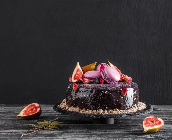 Čokoládový pěnový dort se zrcadlovou polevou zdobený makaróny, fíky, květy na tmavém venkovském pozadí. sváteční dort oslava, zblizka, makro. — Stock fotografie