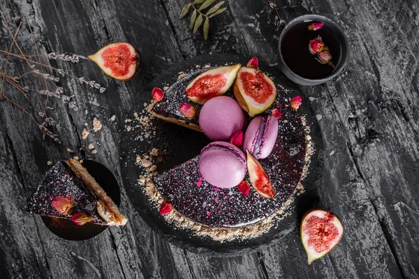 Chocolate mousse cake with mirror glaze decorated with macaroons, figs, flowers on dark rustic background. Holiday cake celebration. Top view, flat lay.