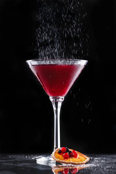 Cold red cocktail with red currant and powdered sugar in tall glass on black background. Summer drinks and alcoholic cocktails in motion. — Stock Photo, Image