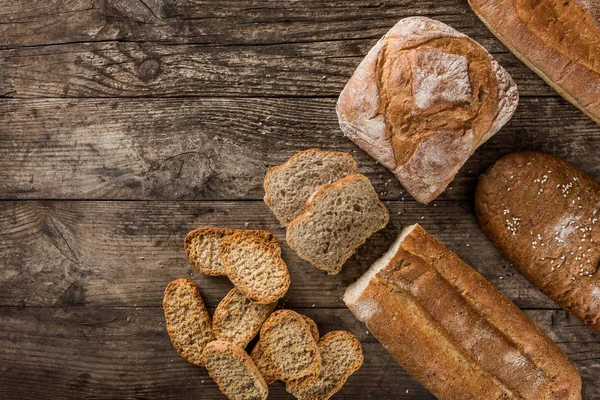 Different fresh bread and spikelets of wheat on rustic wooden ba — Stock Photo, Image