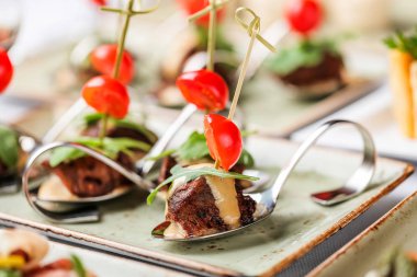 Ziyafet masasında kaşıkla peynir, domates ve yeşillikli ızgara et filetosu kanepeler. Catering gıda, meze tabağı ve atıştırmalıklar.