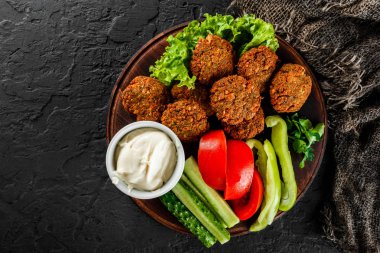 Sarımsaklı yoğurt soslu kavrulmuş nohut falafel köftesi, koyu taş arka plan üzerinde bir tabakta marul ve taze sebze ile servis edilir. Sağlıklı vegan gıda, temiz beslenme, diyet, üst görünümü.