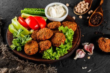 Sarımsaklı yoğurt soslu kavrulmuş nohut falafel köftesi, koyu taş arka plan üzerinde bir tabakta marul ve taze sebze ile servis edilir. Sağlıklı vegan gıda, temiz beslenme, diyet, üst görünümü.