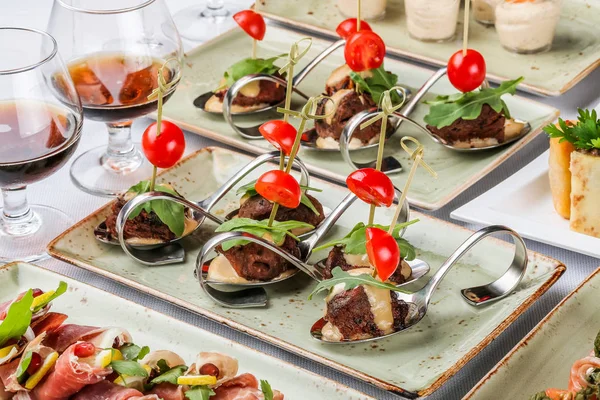 Ziyafet masasında kaşıkla peynir, domates ve yeşillikli ızgara et filetosu kanepeler. Catering gıda, meze tabağı ve atıştırmalıklar