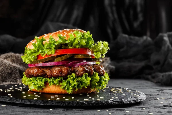 Говяжий бургер с помидорами, красным луком, огурцом и салатом на черном фоне. Нездоровая пища . — стоковое фото
