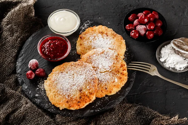Pancake dengan selai buah, ceri, krim asam dan gula icing pada batu tulis hitam dengan latar belakang gelap. Masakan tradisional Rusia pada minggu Pancake atau Shrovetide. Sarapan sehat. Tampilan atas . — Stok Foto