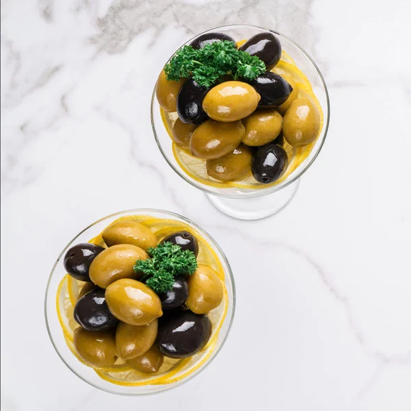 Black and green olives in glass on white marble background. Various kinds of Mediterranean pickled olives. Top view.