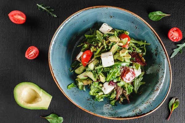 Hälsosam fräsch sallad med avokado, greener, ruccola, spenat, körsbärstomater och ost i plåt över mörkt bord. Hälsosam veganmat, rent ätande, bantning, topp v. IEW — Stockfoto