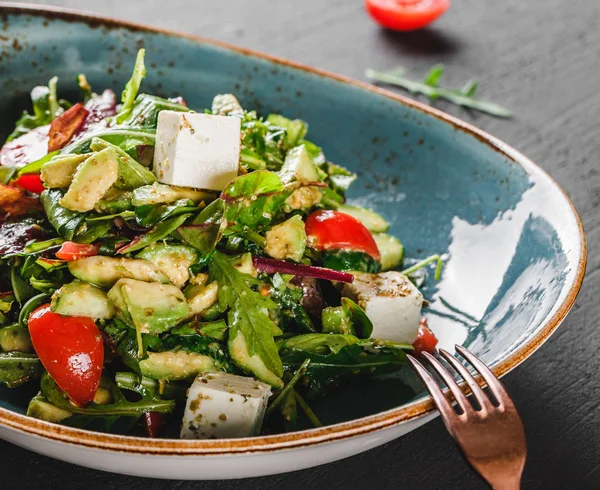 Hälsosam fräsch sallad med avokado, greener, ruccola, spenat, körsbärstomater och ost i plåt över mörkt bord. Hälsosam vegansk mat, rent ätande, bantning. — Stockfoto