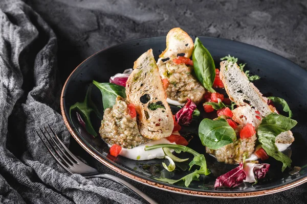 Gesunder Salat aus gegrillten Auberginen, Rucola, Spinat, Tomaten, Croutons und Soße in einem Keramikteller vor grauem Hintergrund. Gesunde vegane Ernährung, saubere Ernährung, Ernährung, Nahaufnahme — Stockfoto