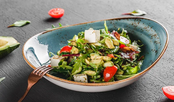 Ensalada fresca saludable con aguacate, verduras, rúcula, espinacas, tomates cherry y queso en plato sobre mesa oscura. Comida vegana saludable, alimentación limpia, dieta . — Foto de Stock