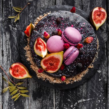 Aynalı kremalı çikolatalı pasta. Makaronlarla, incirlerle, koyu kırsal arka planda çiçeklerle süslenmiş. Tatil pastası kutlaması. Üst manzara, düz uzanma