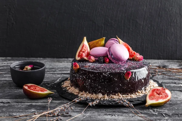 マカロン、イチジク、暗い素朴な背景に花で飾られたミラー釉薬とチョコレートムースケーキ。ホリデーケーキのお祝い、終わり — ストック写真