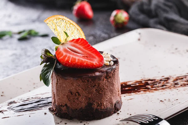 Läcker chokladcheesecake med jordgubb och mynta på tallrik över grå bakgrund. — Stockfoto
