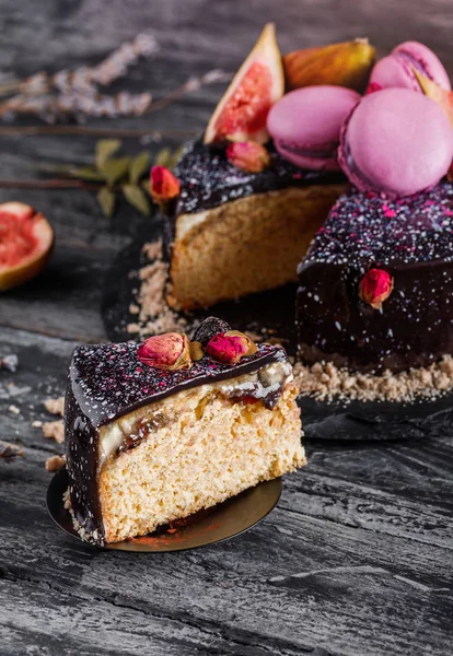 Chocolate mousse cake with mirror glaze decorated with macaroons, figs, flowers on dark rustic background. Holiday cake celebration, close up