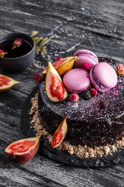 Choklad mousse kaka med spegel glasyr dekorerad med makaroner, fikon, blommor på mörk rustik bakgrund. Semester tårta fest, närbild — Stockfoto