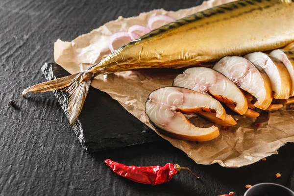 Aperitivo peixe de cavala defumado com especiarias, pimenta e pão em papel artesanal sobre fundo de pedra escura. Comida mediterrânica, peixe de arenque, frutos do mar, close — Fotografia de Stock