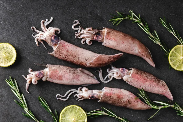Свіжі сирі цілі кальмари зі спеціями, розмарином та лаймом на темній стрічці — стокове фото