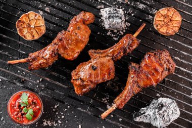 Grilled lamb ribs meat or rib eye with tomato sauce over the coals on a barbecue, dark background. Top view clipart
