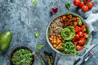 Fırında patates, nohut, kinoa, domates, roka, avokado, açık mavi arka planda peçeteli lahanalı Buda kasesi salatası. Sağlıklı vejetaryen yemekleri, temiz yemek, perhiz, üst manzara.