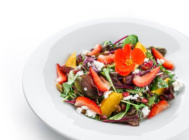 Mix yeşillik, çilek, portakal, fındık, krem peynir ve izole beyaz arka plan tabakta yenilebilir çiçekler ile Sağlıklı taze salata. Sağlıklı gıda, vejetaryen diyet, yakın çekim