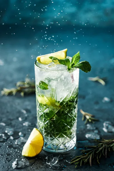 Fresh Mojito cocktail with lime, rosemary, mint and ice in jar glass on dark blue background. Studio shot of drink in freeze motion, drops in liquid splash. Summer cold drink and cocktail — Stock Photo, Image