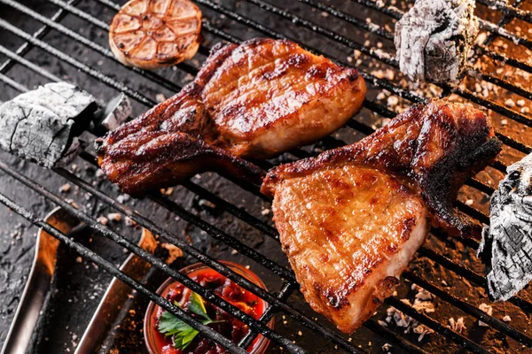 Стейк-мясо на гриле с чесноком на углях на барбекю, темный фон со светом огня. Вид сверху — стоковое фото