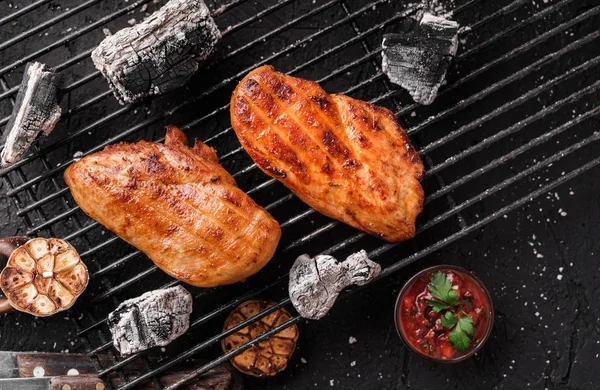 Gegrilltes Hähnchenbrustfleisch mit Knoblauch über den Kohlen auf dem Grill, dunkler Hintergrund mit Feuerschein. Ansicht von oben — Stockfoto