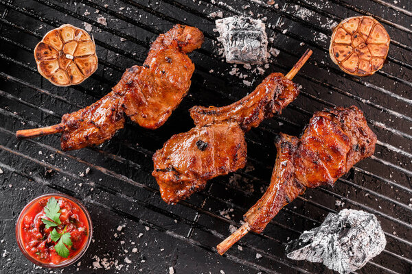 Grilled lamb ribs meat or rib eye with tomato sauce over the coals on a barbecue, dark background. Top view