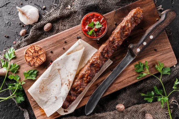 Kebab de viande grillé dans du pain pita avec sauce tomate sur une planche d'ardoise sur fond sombre. Vue du dessus — Photo