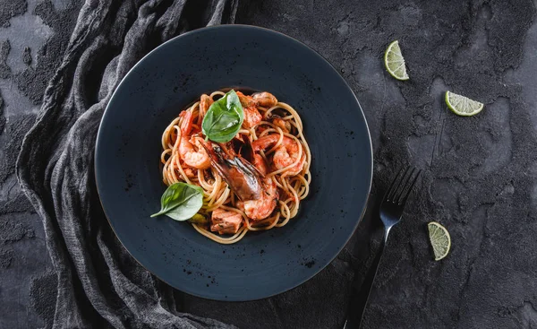 Pasta spaghetti with seafood, langoustine, mussels, oysters, shrimp, salmon fillet in sauce with herbs in plate over dark grey background. Italian food, top view