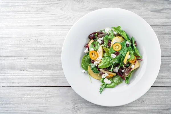 Gesunder frischer Salat mit Gemüsemischung, Apfel, Frischkäse, Preiselbeere, Sauce und essbaren Blumen in einem Teller auf hellem Holzgrund. gesunde Ernährung, vegetarische Ernährung, Draufsicht — Stockfoto