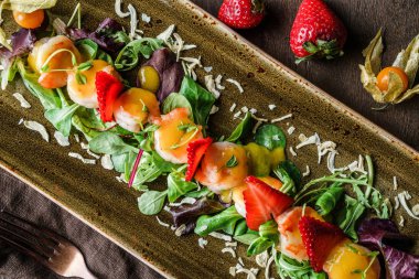 Keten peçete ile kahverengi ahşap arka plan üzerinde plaka karışık yeşillik, çilek, physalis ve karides ile Sağlıklı taze salata. Sağlıklı gıda, temiz beslenme, diyet, üst görünüm