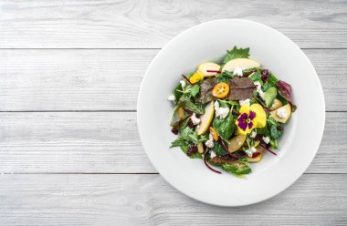Mix yeşillik, elma, krem peynir, kızılcık, sos ve hafif ahşap arka plan tabaktabak yenilebilir çiçekler ile Sağlıklı taze salata. Sağlıklı gıda, vejetaryen diyet, üst görünümü