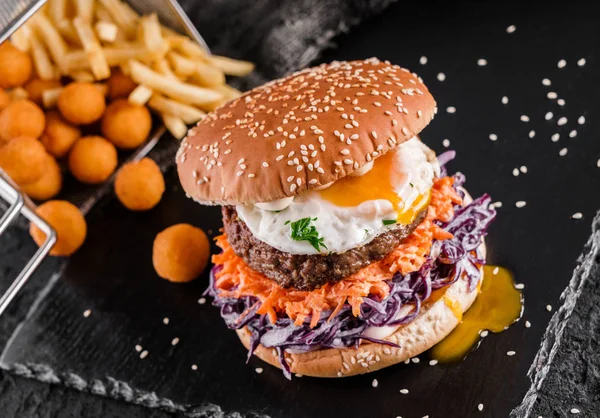 Hamburger di manzo con cavolo, carota, uova fritte, salsa e polpette fritte, patatine fritte su sfondo nero ardesia, vista dall'alto — Foto Stock