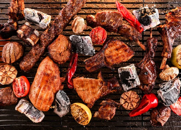 Różne pyszne grillowane mięso z warzywami na węglu na grillu, ciemne tło ze światłem ognia. Widok z góry — Zdjęcie stockowe