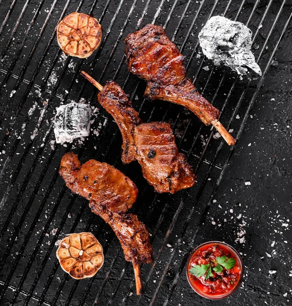 Жареные ребрышки баранины или ребрышки с томатным соусом на углях на барбекю, темный фон. Вид сверху — стоковое фото
