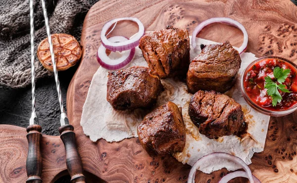 Viande grillée ou kebab shish, shashlik avec sauce tomate sur une planche de bois sur fond de pierre sombre. Vue du dessus — Photo