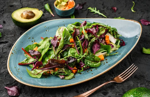 Ensalada verde fresca con verduras mixtas, rúcula de espinacas, calabaza, aguacate en plato sobre fondo oscuro. Comida saludable, alimentación limpia, dieta vegana, vista superior — Foto de Stock