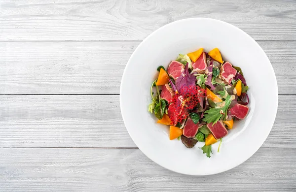 Gesunder Salat mit gebratenem Thunfisch, Gemüse, Paprika und Soße im Teller auf hellem Holzgrund. gesunde Ernährung, saubere Ernährung, Diät, Draufsicht — Stockfoto