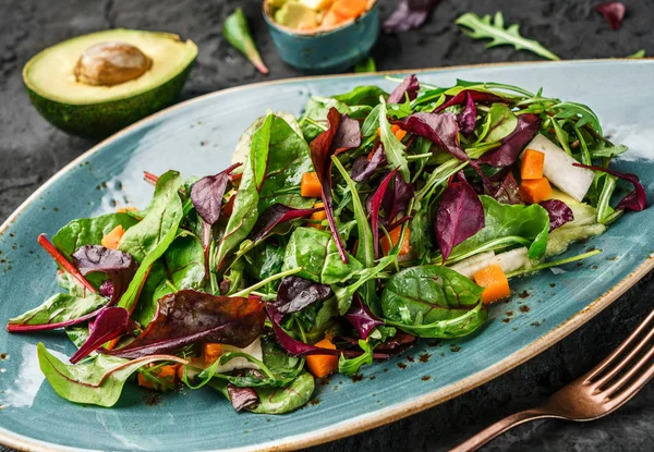 Frischer grüner Salat mit gemischtem Gemüse, Spinat Rucola, Kürbis, Avocado im Teller vor dunklem Hintergrund. gesunde Ernährung, saubere Ernährung, vegane Ernährung, Draufsicht — Stockfoto