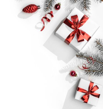 Kırmızı kurdeleli hediye kutularıyla Noel köknar dalları beyaz arka planda bokeh, ışık. Noel ve yeni yıl tebrik kartı, kış tatili. Düz, üst görünüm, sert gölge.