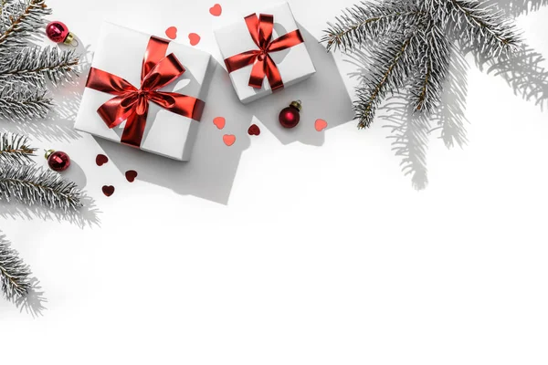 白い紙の背景に赤リボンでギフトボックスとクリスマスモミの枝はボケ、光。クリスマスと新年の挨拶カード、冬の休日。フラットレイアウト、トップビュー、過酷な影 — ストック写真