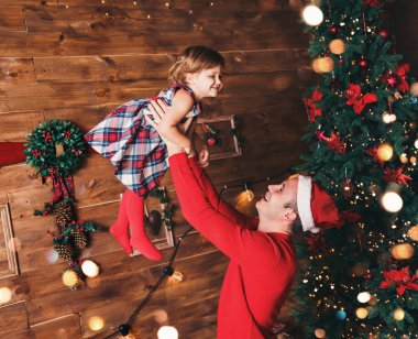Mutlu Noeller ve mutlu yıllar! Baba ve kızı, Noel ağacı ve Noel hediyesi kutularıyla süslenmiş bir şekilde oturma odasında gülümsüyor. Portre seven aile yakın çekim, tatil